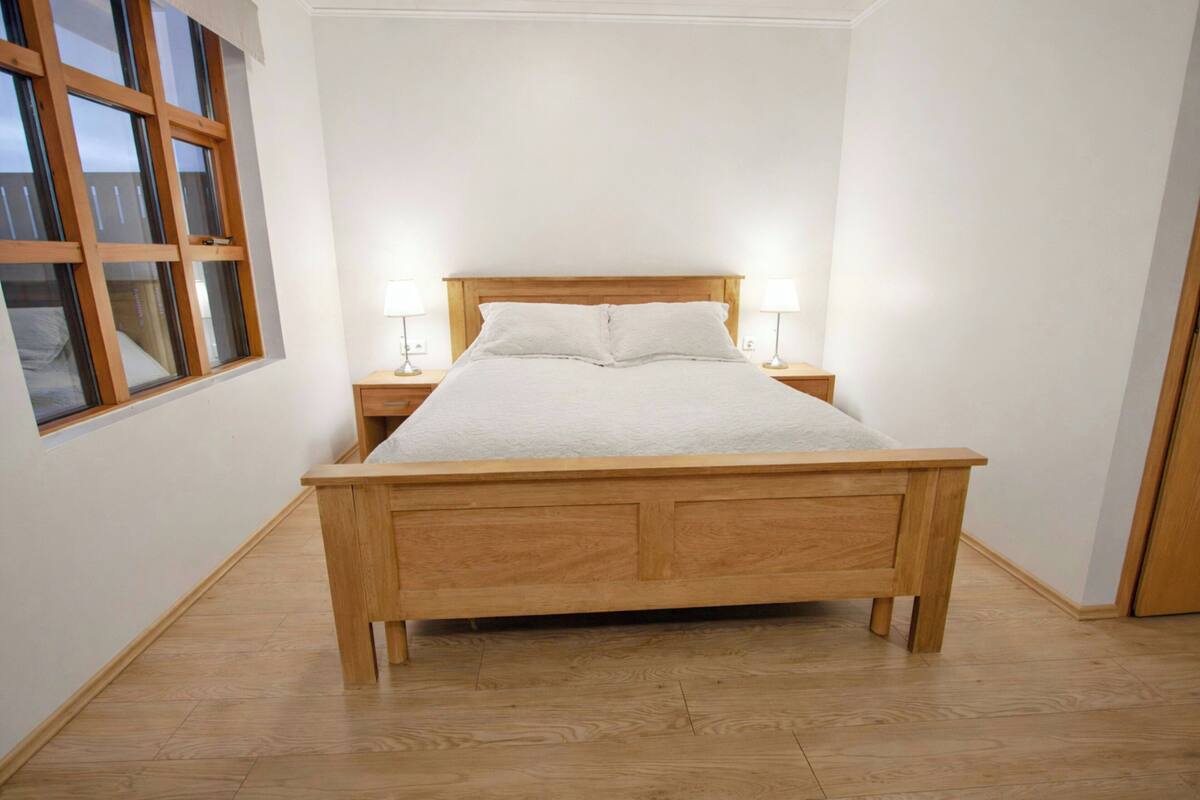 A wooden bed with white bedding in a room with white walls and a wooden floor.