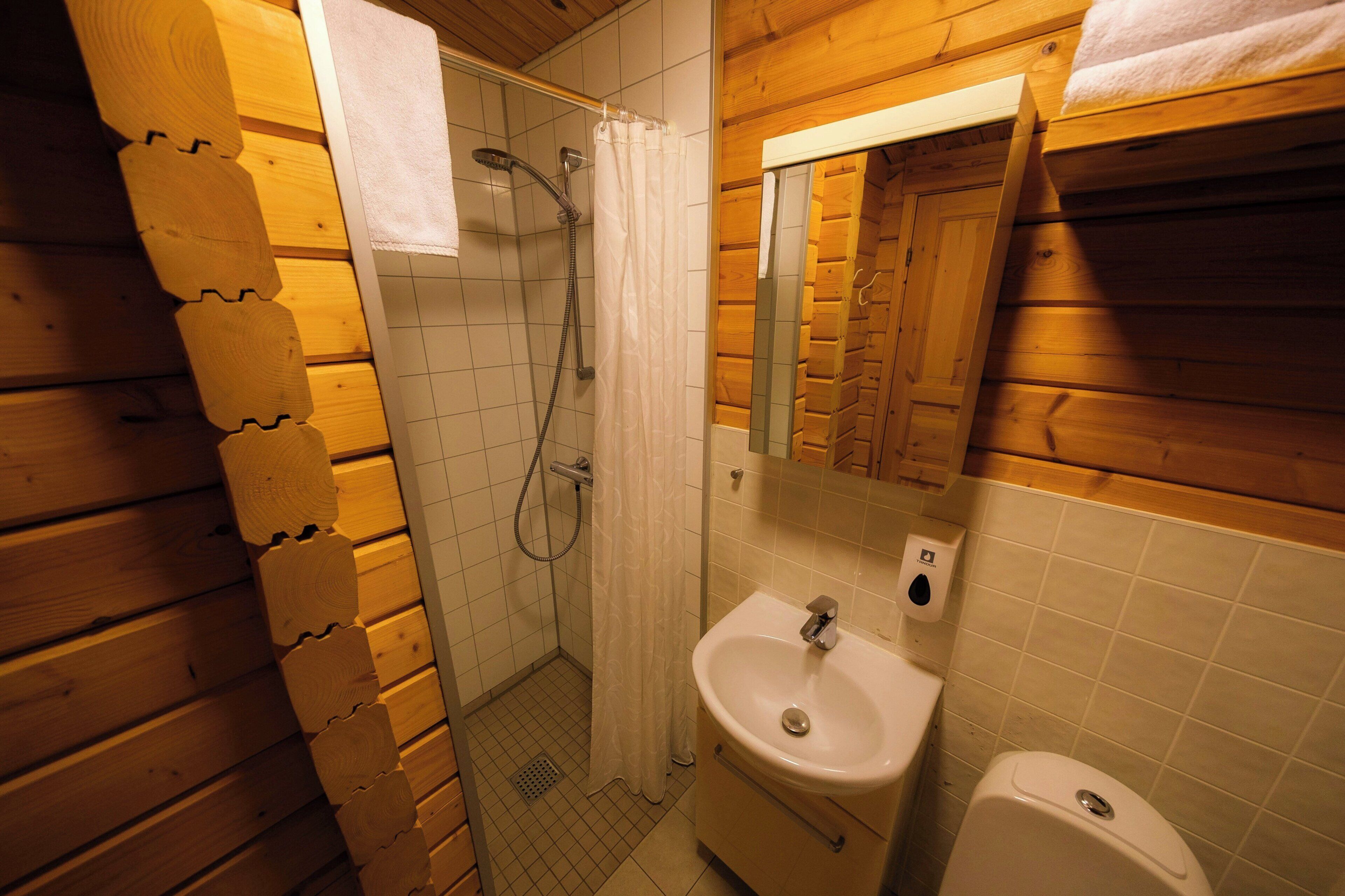 Baño de cabaña de madera con ducha, lavamanos e inodoro.