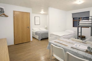 Quarto com duas camas, uma porta de madeira, uma mesa com cadeiras e uma cama beliche.