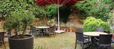 An outdoor patio with round tables and chairs, surrounded by potted plants and a stone wall.