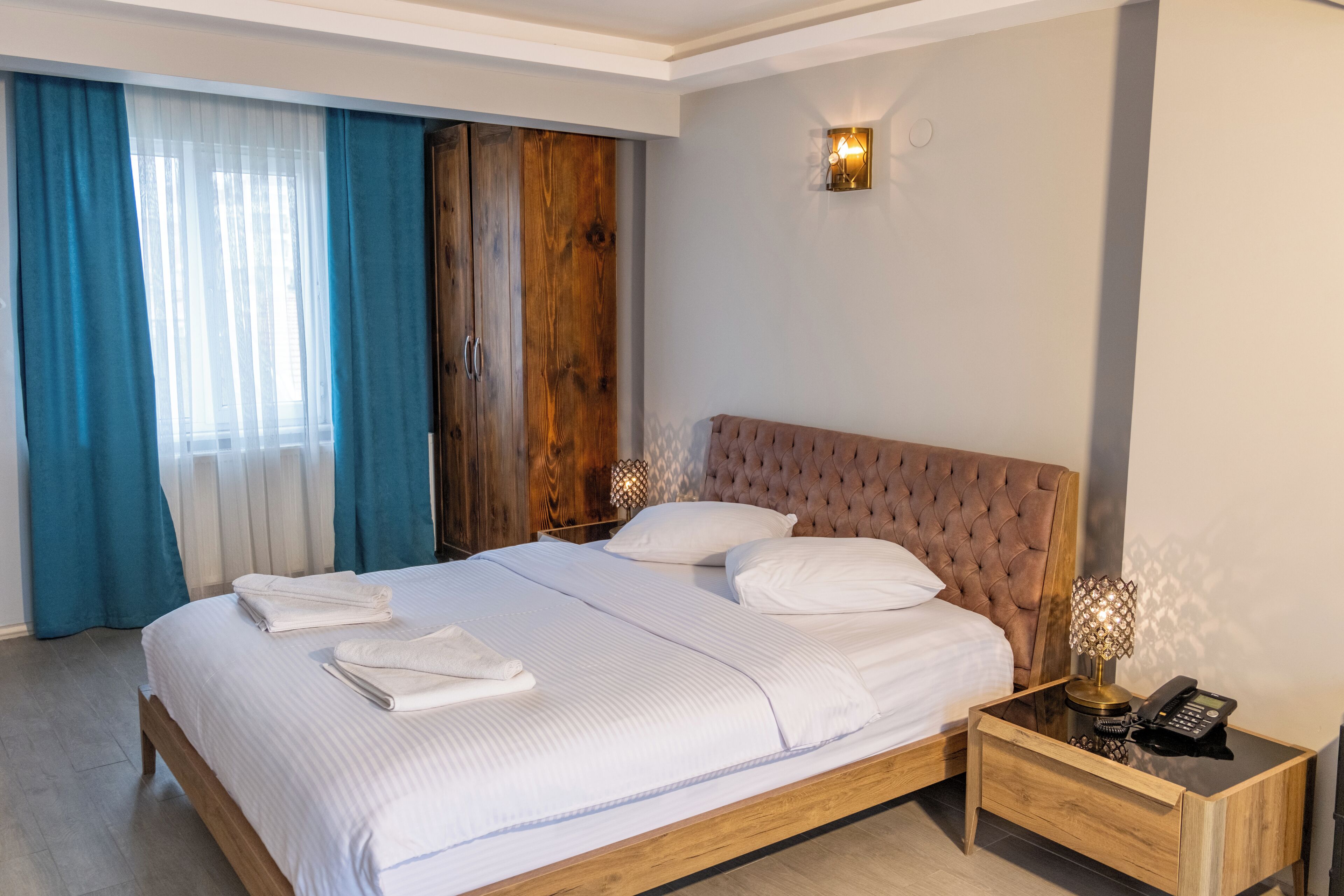 A neatly made bed with white linens, a wooden headboard, and a bedside table with a lamp and phone.