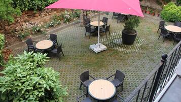 Un espacio de patio al aire libre con mesas y sillas redondas, un paraguas rosa grande y plantas en macetas.