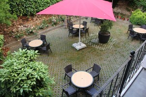 Un espacio de patio al aire libre con mesas y sillas redondas, un paraguas rosa grande y plantas en macetas.