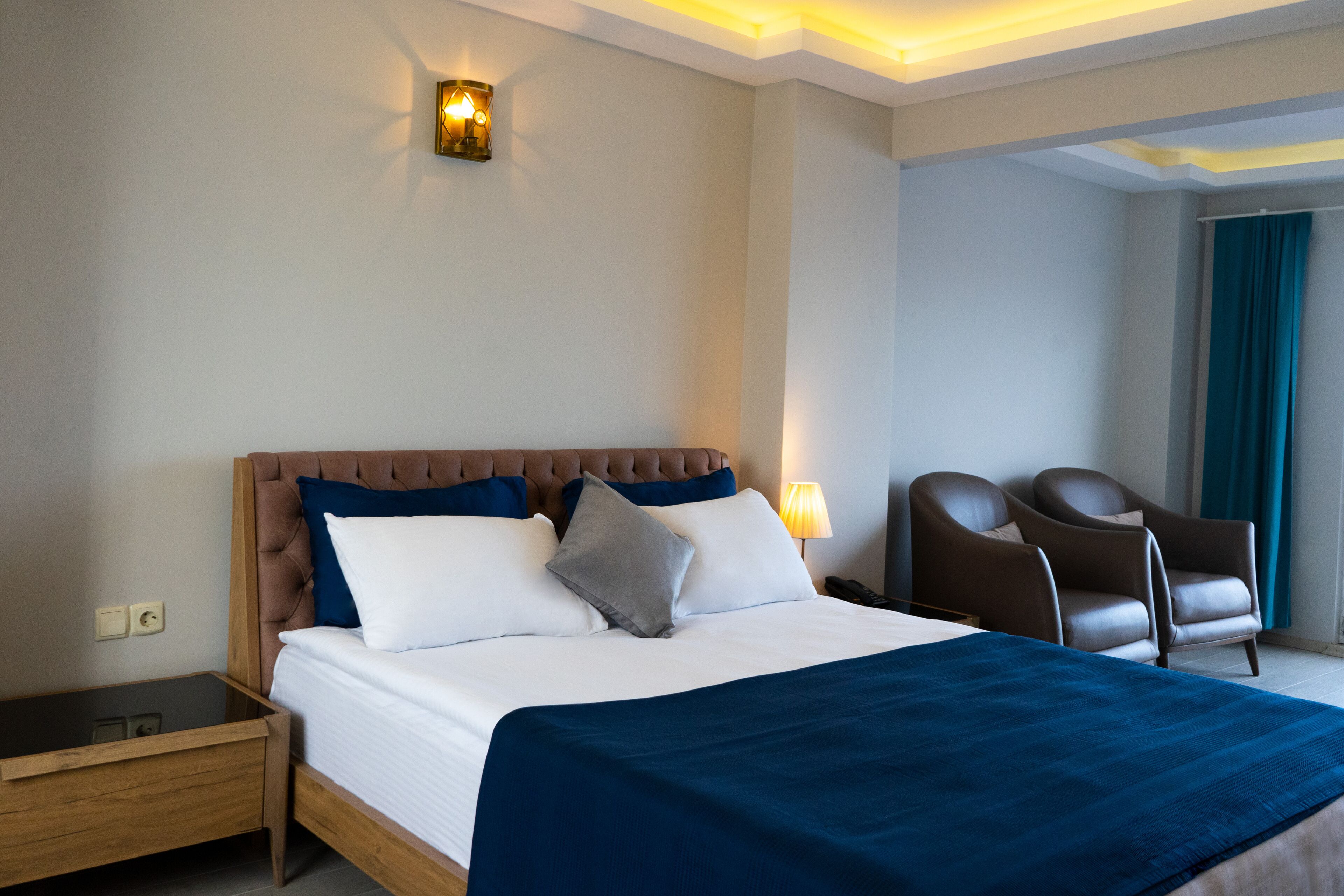Une chambre d’hôtel avec un grand lit, une table de chevet, une chaise et une lampe fixée au mur.