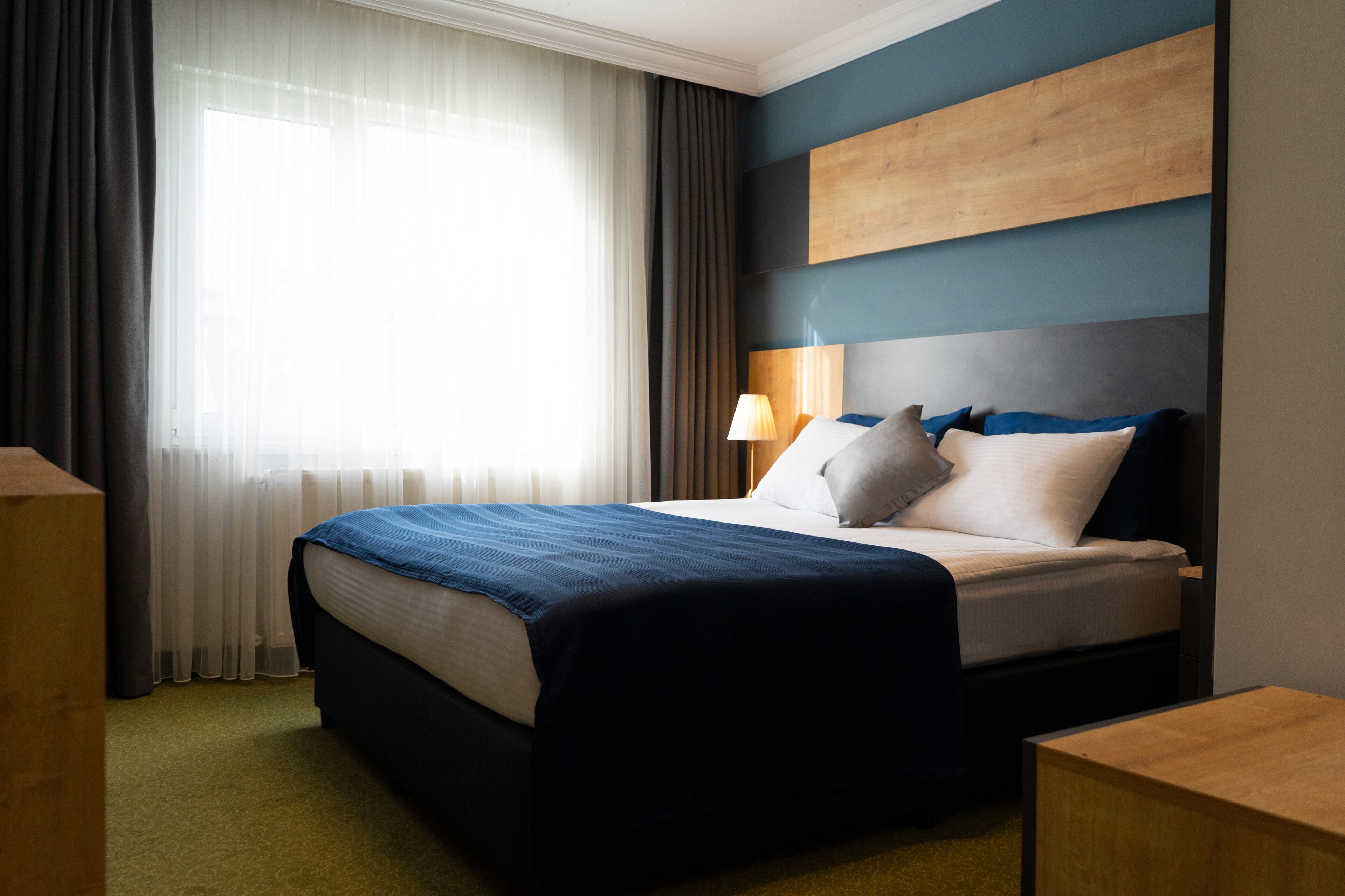 Ein Hotelzimmer mit einem Bett, einem Nachttisch, einer Lampe und einem Fenster mit Vorhängen.