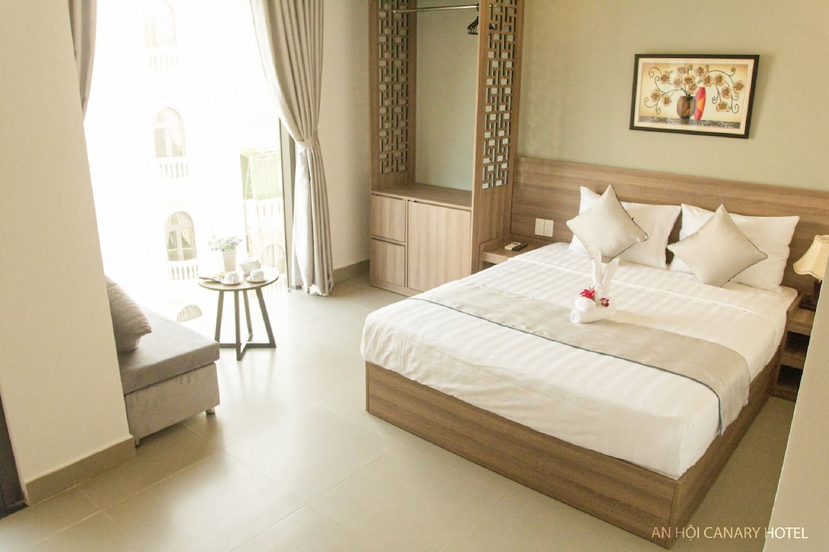 A hotel room with a large bed, a bedside table, a wardrobe, and a view of the outside.