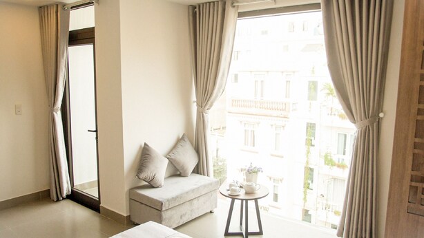 A hotel room with a sofa, a small table with a teapot, and a view of buildings through large windows. - An Hoi Canary Hotel (Da Nang)