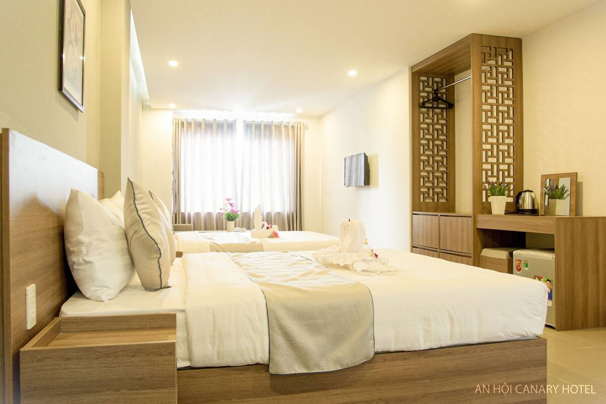A hotel room with two beds, a wooden wardrobe, a small desk, and a window with curtains.