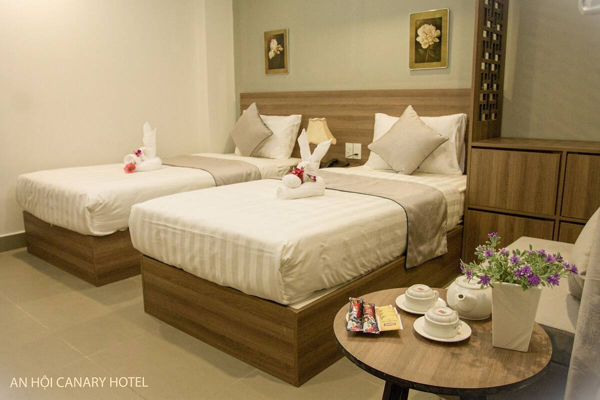 A hotel room with two beds, a small table with tea sets, and a vase with flowers.