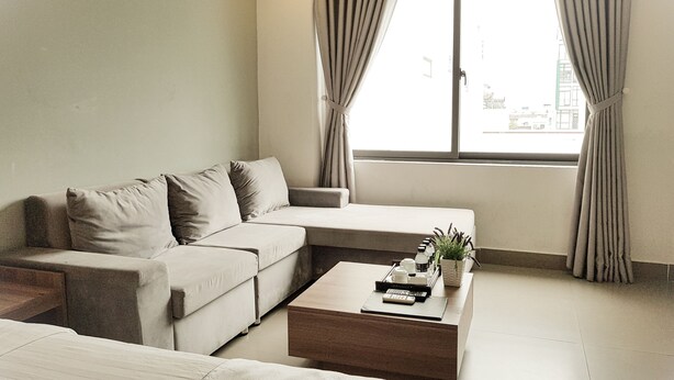 A modern living room with a sofa, a coffee table, and a window with curtains. - An Hoi Canary Hotel (Da Nang)