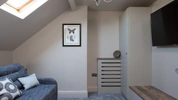 A modern bedroom with a sloped ceiling, a skylight, a framed butterfly artwork, a bedside table with a mirror, and a TV mounted on the wall.