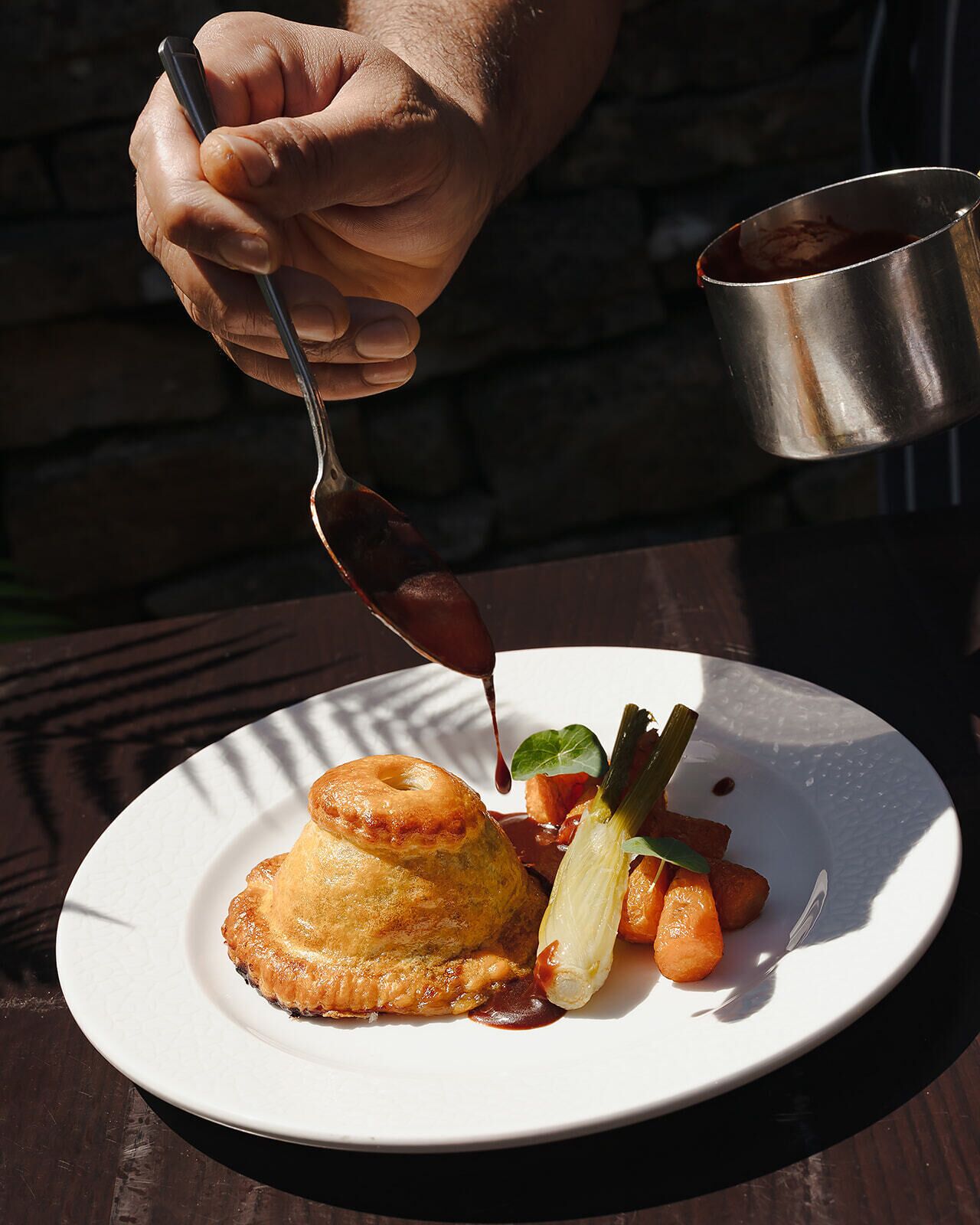 A person pouring sauce onto a plate with food.