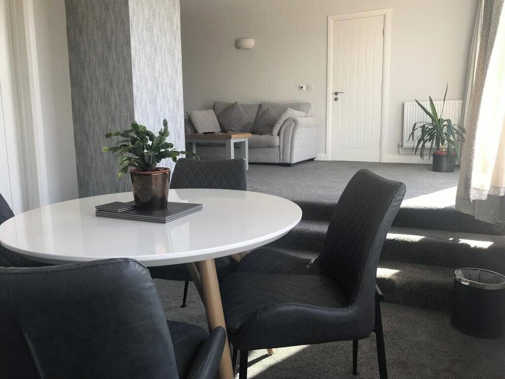A modern living room with a round white table, black leather chairs, a grey sofa, and a white door.
