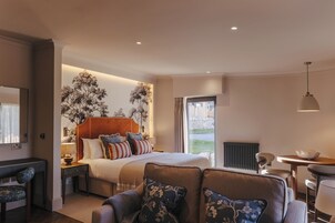 A modern bedroom with a large bed, a sofa, a desk, and a view of the outdoors.