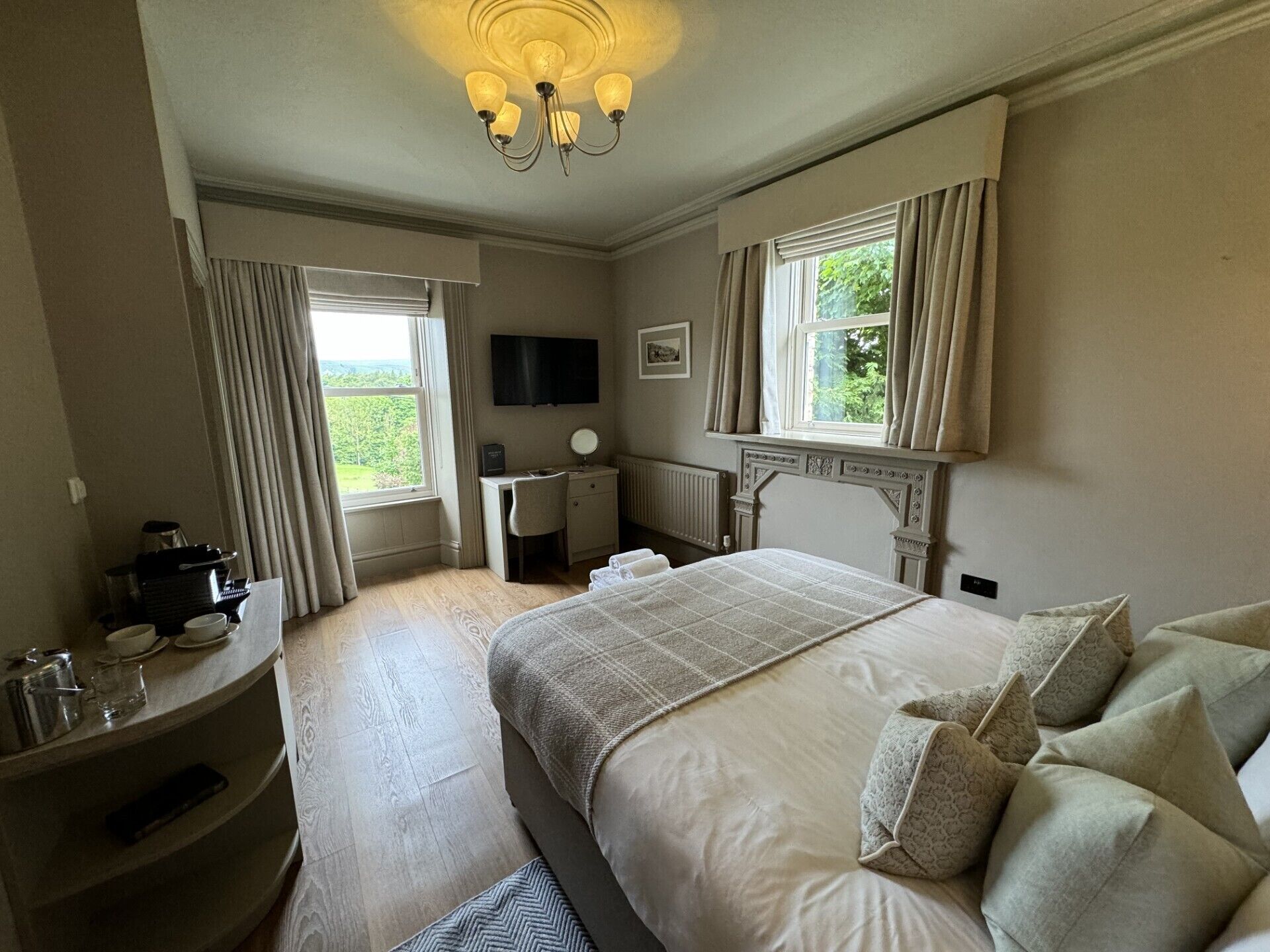 A bedroom with a large bed, a desk, a chair, a television, and a window with curtains.