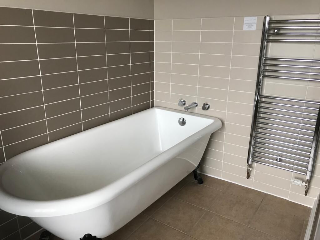 Un bagno con una vasca da bagno bianca, un porta asciugamani cromato e pareti piastrellate color beige.