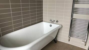 Un bagno con una vasca da bagno bianca, un porta asciugamani cromato e pareti piastrellate color beige.