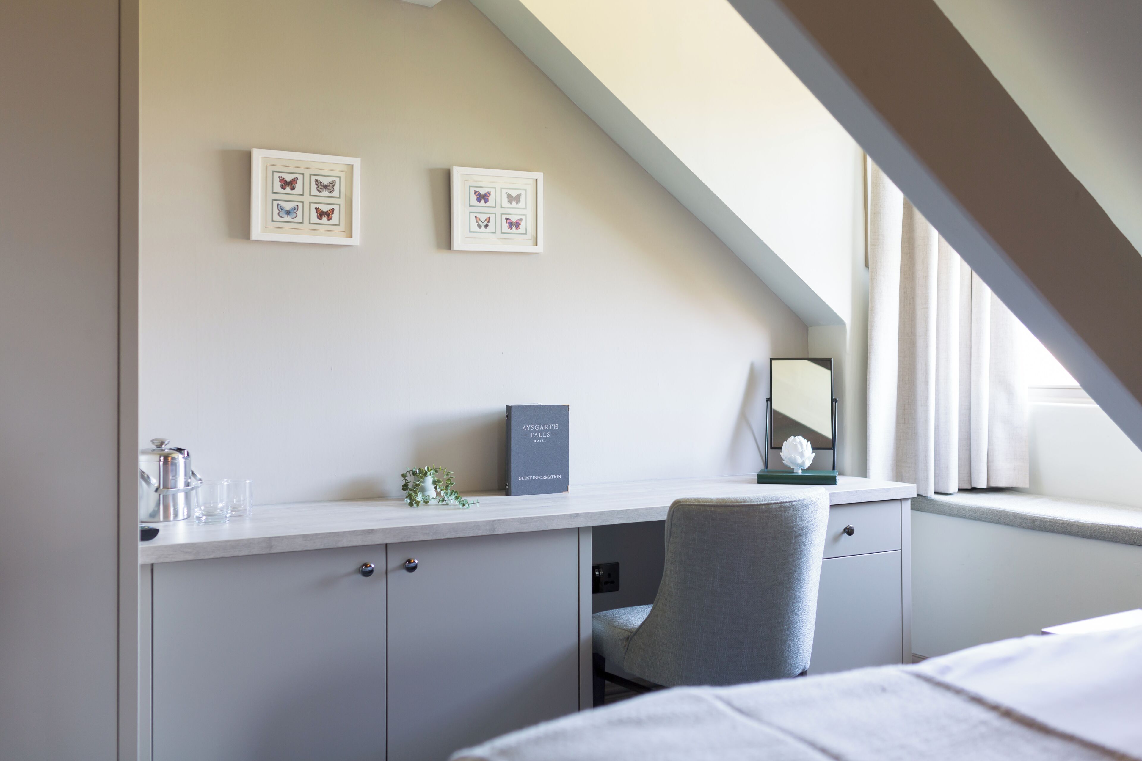 Ein Schlafzimmer mit Bett, Schreibtisch, Stuhl, Fenster und gerahmten Schmetterlingsbildern an der Wand.