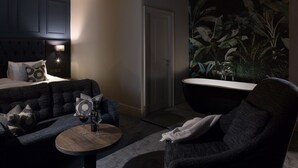 A modern room with a dark blue upholstered sofa, a round wooden coffee table, and a black bathtub. - Aysgarth Falls Hotel (Leyburn)