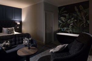 Una habitación moderna con un sofá tapizado azul oscuro, una mesa de centro redonda de madera y una bañera negra.