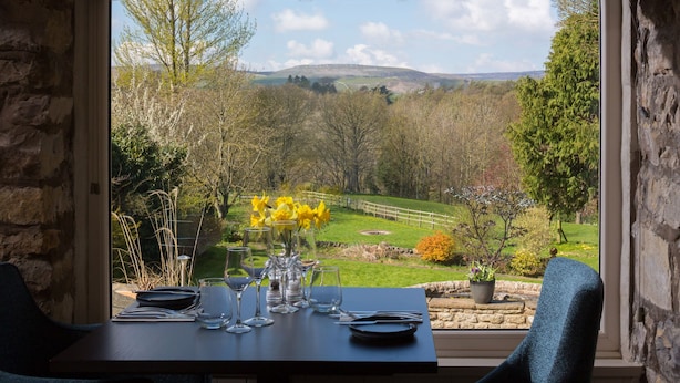 A dining table set for two with a view of a lush garden and hills in the background. - Aysgarth Falls Hotel (Leyburn)