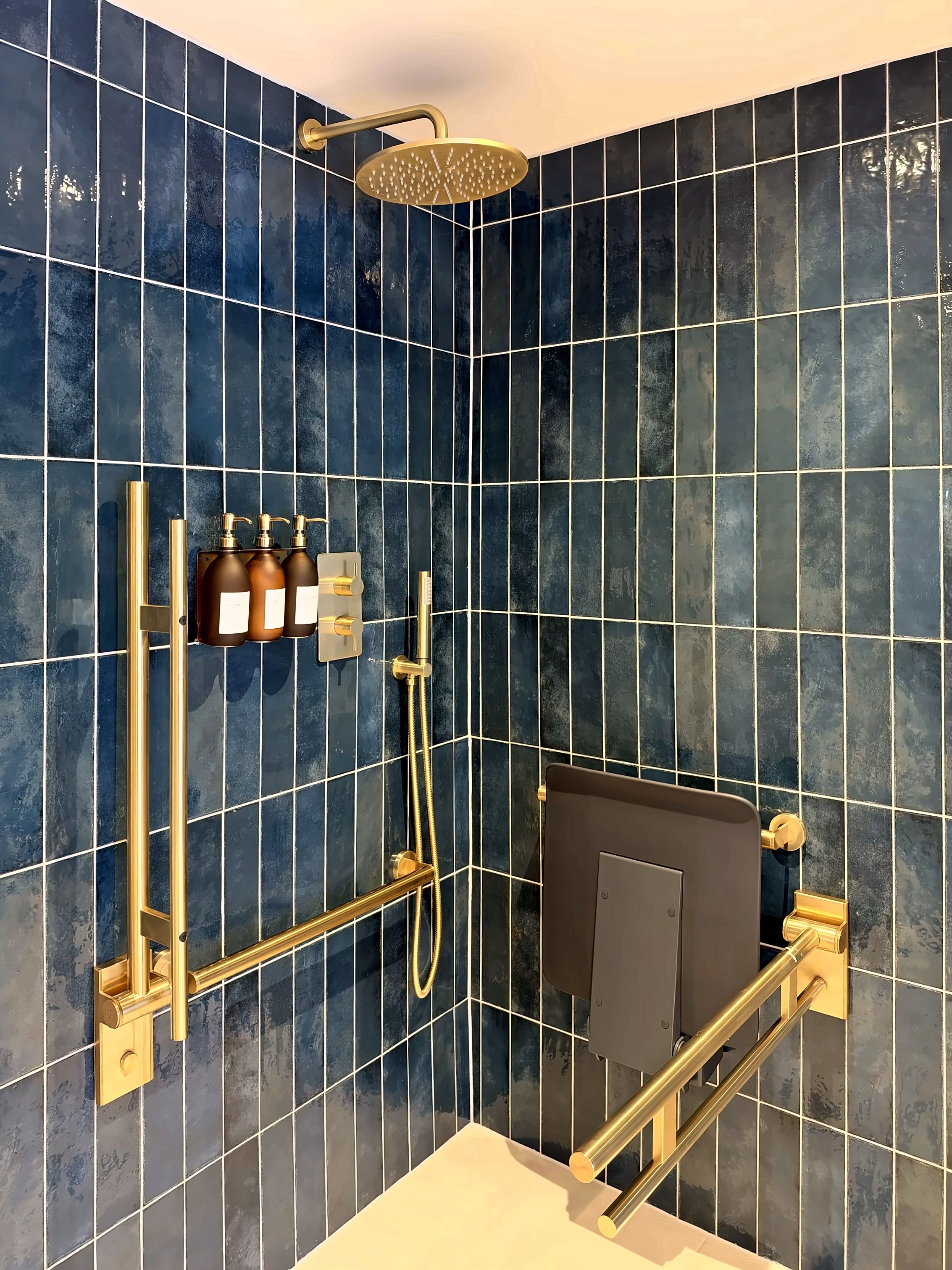 A modern bathroom with a shower, golden fixtures, and dark blue tiles.