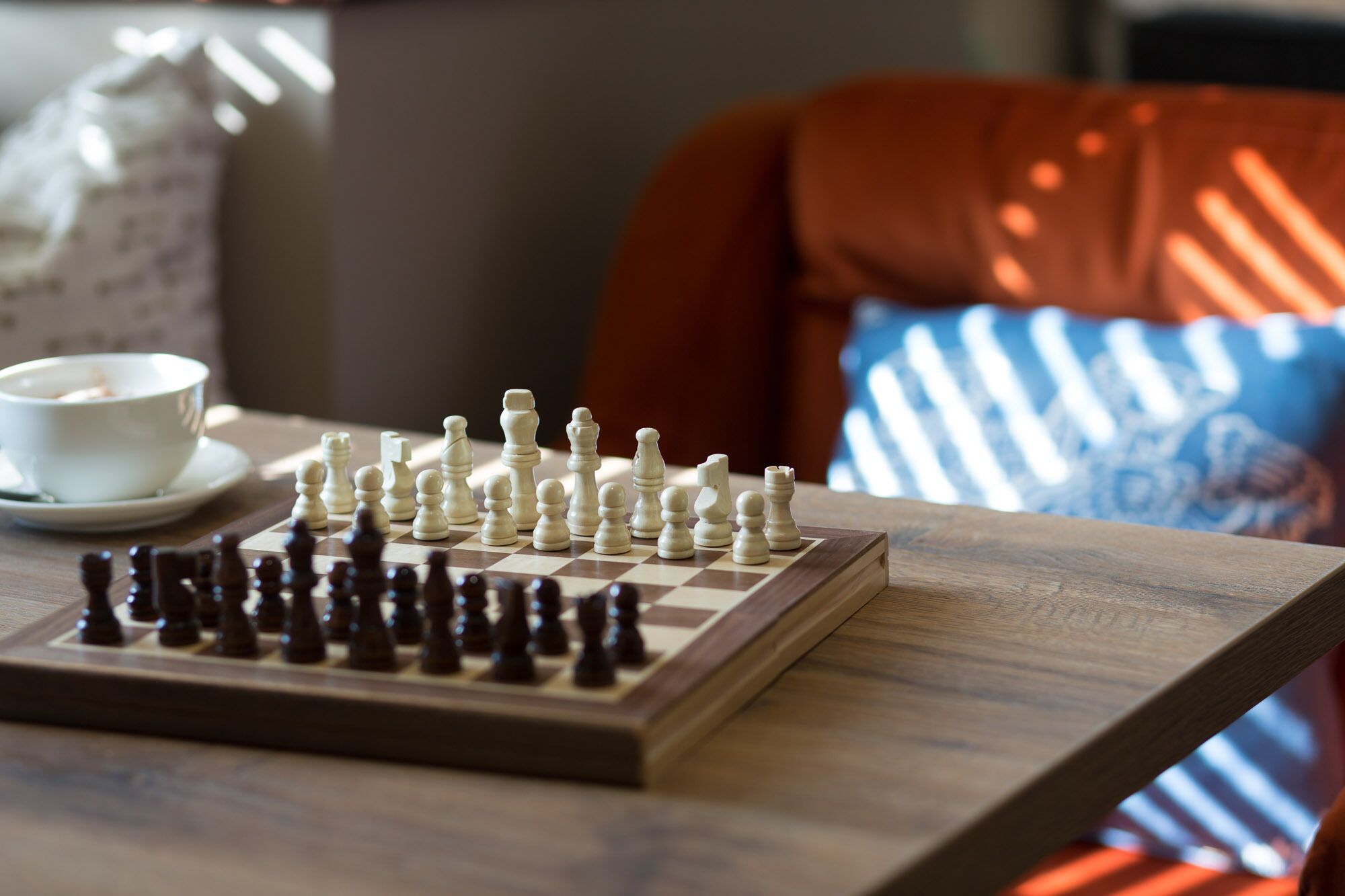 A chessboard on a wooden table with a cup and saucer beside it.