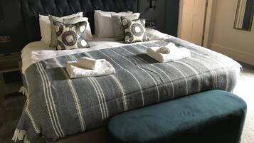 Una cama bien tendida con un edredón a rayas y dos almohadas, un cabecero oscuro y un banco color turquesa.