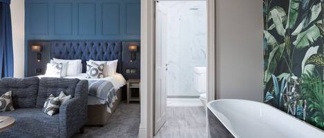 A modern bedroom with a large bed, a sitting area, and a bathroom with a freestanding tub.