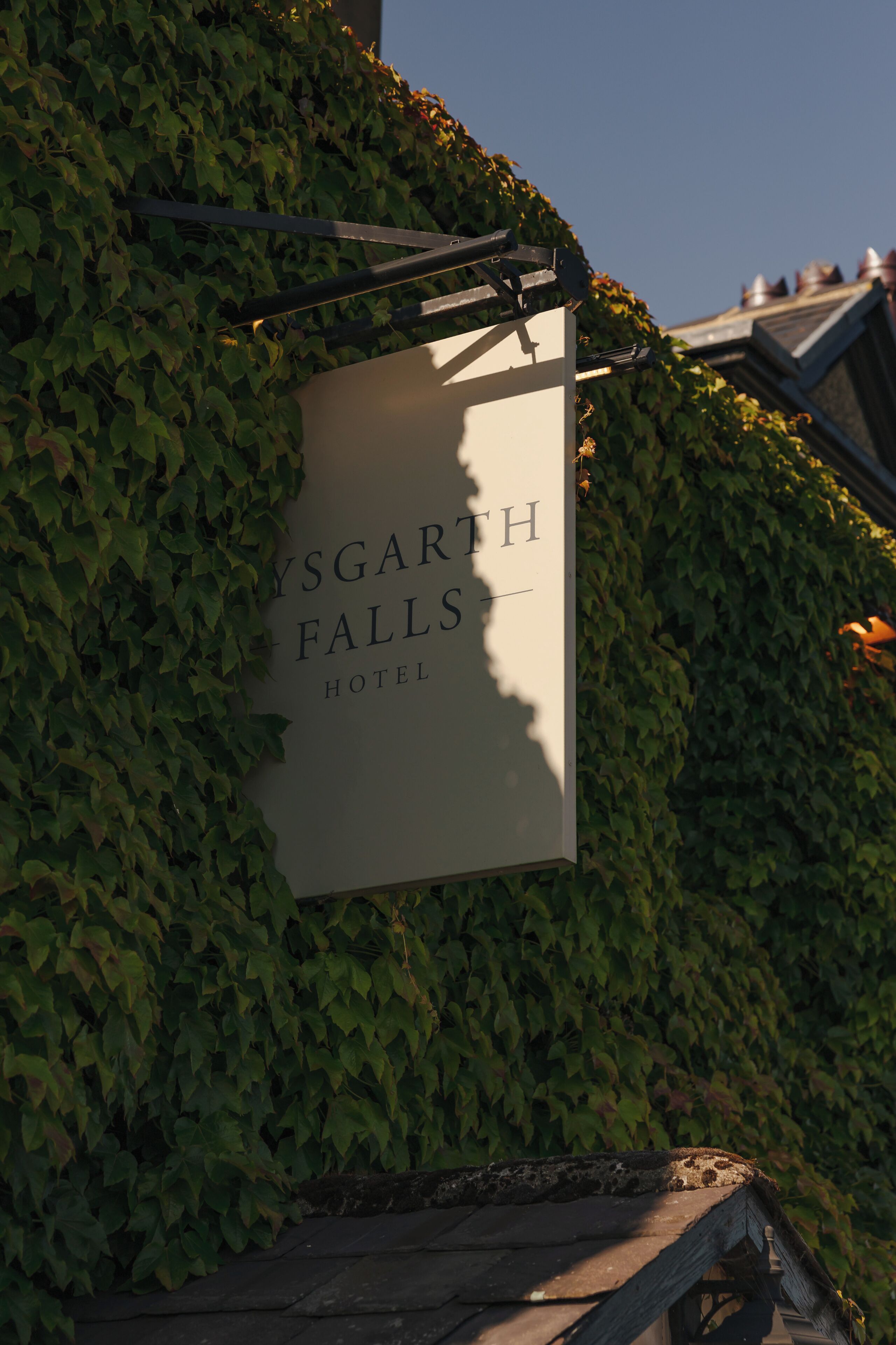 A sign for 'YSGARTH FALLS HOTEL' mounted on a wall covered with ivy.