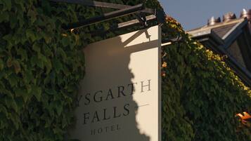 A sign for 'YSGARTH FALLS HOTEL' mounted on a wall covered with ivy.