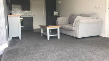 Um espaço compacto com um sofá cinzento, uma mesa pequena branca e uma área de kitchenette.