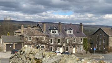 A stone building with multiple windows and a garage, surrounded by a stone wall and parked cars.
