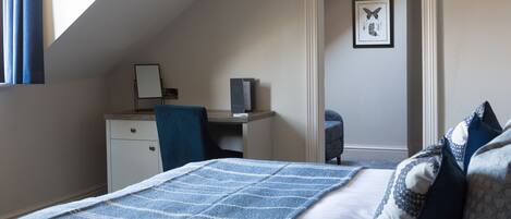 A bedroom with a bed, a desk, and a chair. There is a framed picture on the wall.
