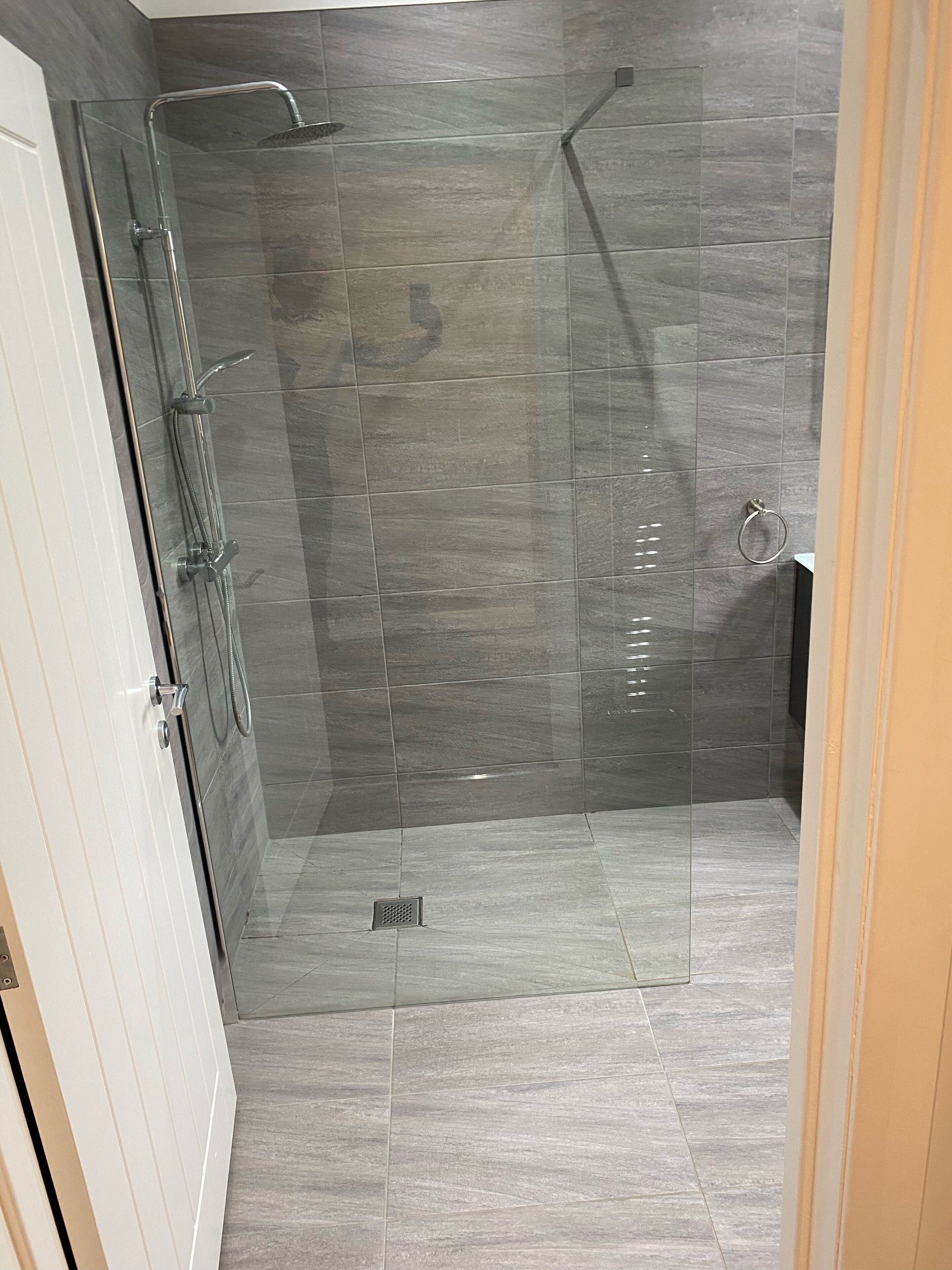 A modern shower area with a glass door, a handheld showerhead, and a wall-mounted faucet.
