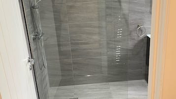 A modern shower area with a glass door, a handheld showerhead, and a wall-mounted faucet.