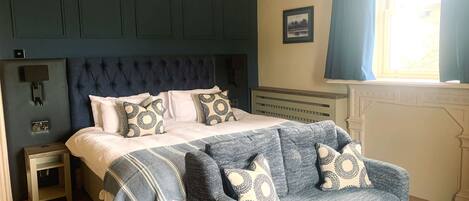 A bedroom with a large bed, a dark headboard, a blue sofa, and a small round table.