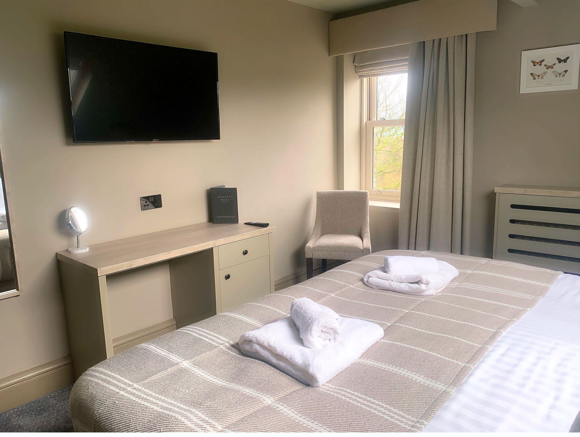 A hotel room with a bed, a desk, a chair, a TV, and a window with curtains.