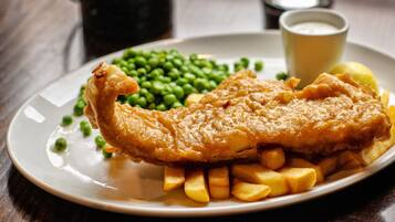 Ein Teller mit Fisch und Pommes, Erbsen und einer kleinen Soße.