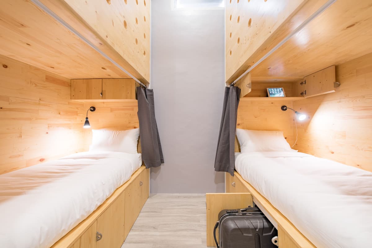 A compact room with two wooden bunk beds, each with a small shelf and a light fixture above.