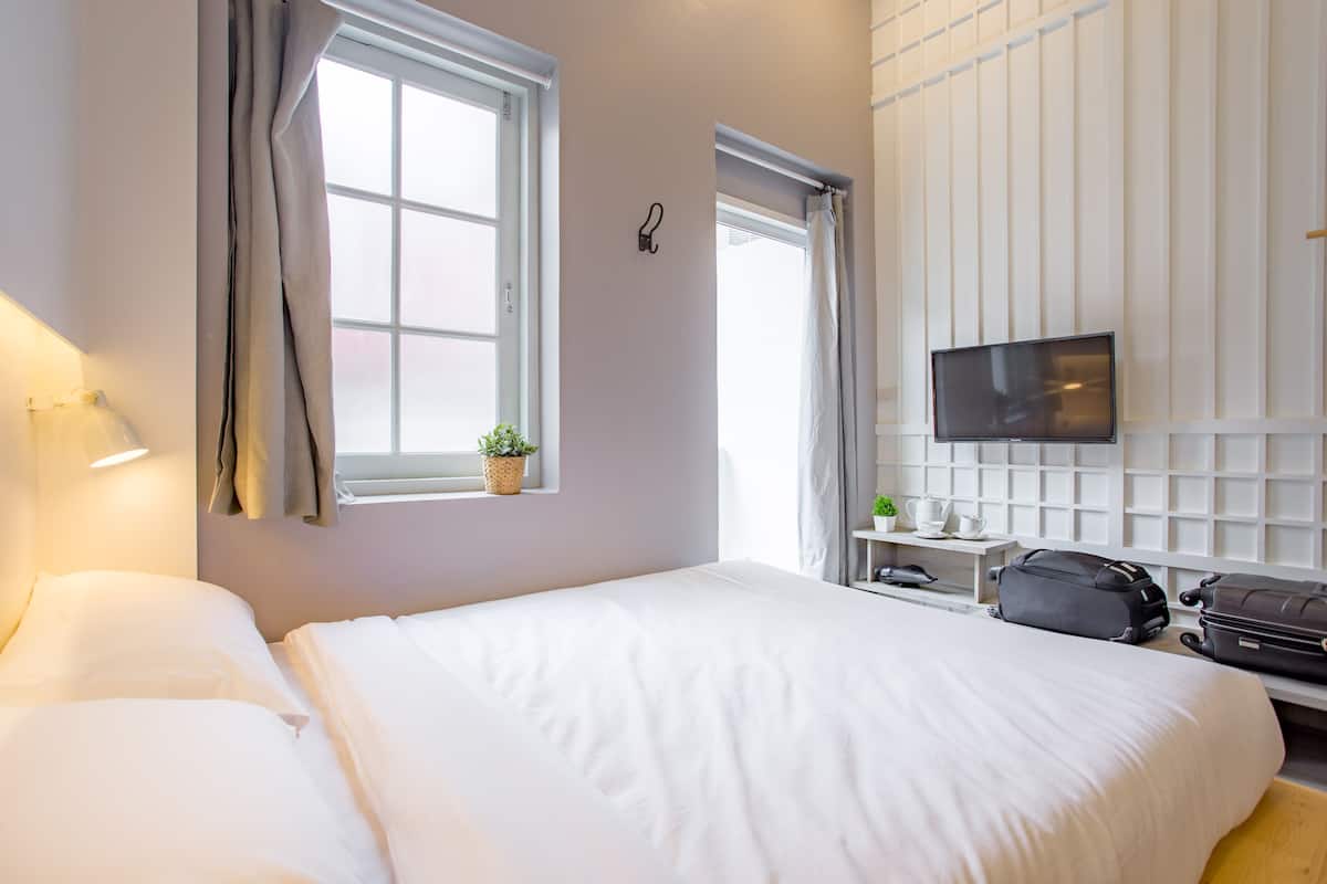 A hotel room with a bed, a TV, a desk with a computer, and a window with curtains.