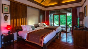 A hotel room with two beds, wooden flooring, a ceiling with wooden beams, a nightstand with a lamp, and a window with a view of greenery.