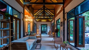 A spacious hallway with a wooden ceiling, large windows, and a seating area with a sofa and chairs.