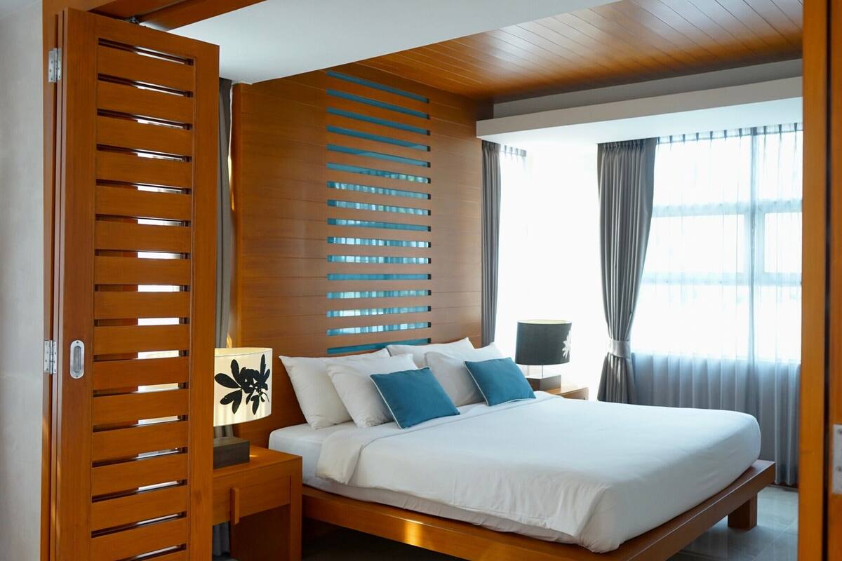 Une chambre d’hôtel moderne avec un cadre de lit en bois, du linge de lit blanc et une table de chevet avec une lampe.