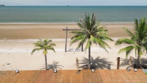 A beach view with palm trees and a wooden deck with lounge chairs.