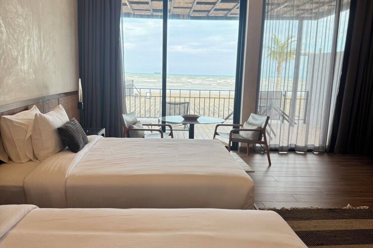 Une chambre d’hôtel avec un grand lit, une petite table, deux chaises et une vue sur la plage.