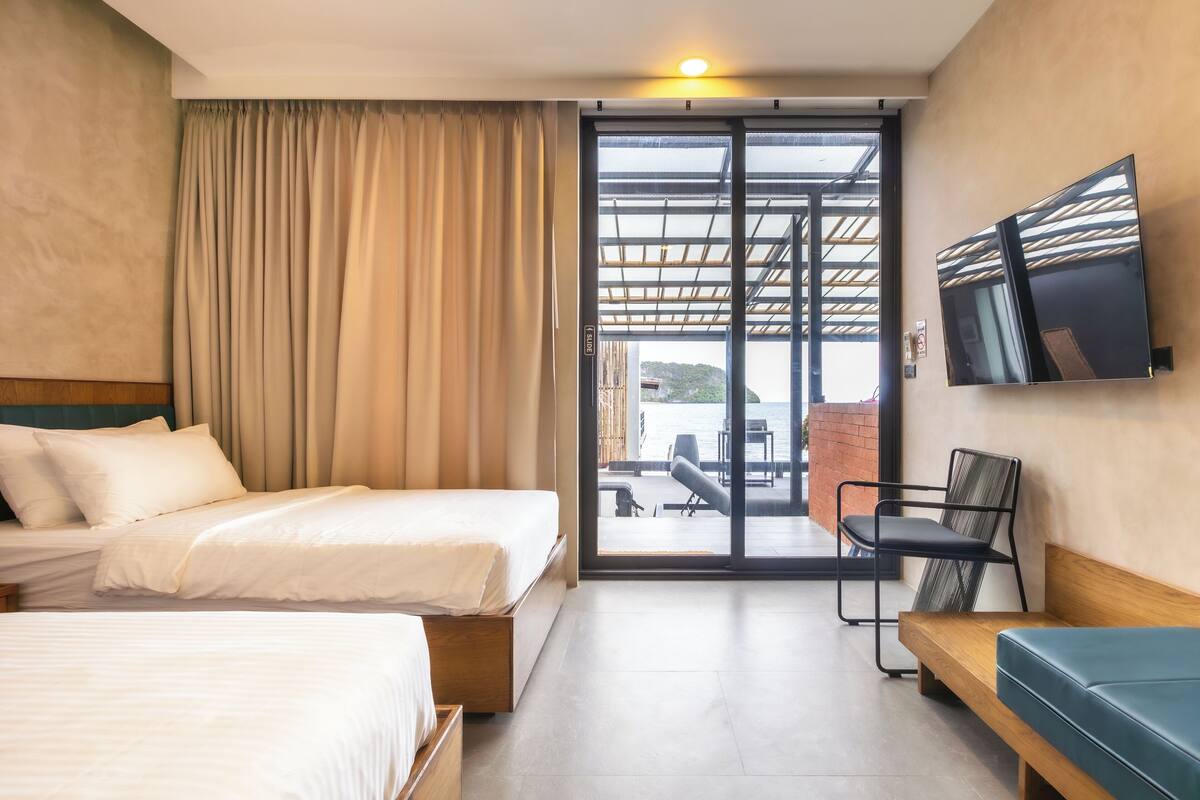 Une chambre d’hôtel avec deux lits, une télévision, une porte-fenêtre coulissante donnant sur un balcon et une chaise.