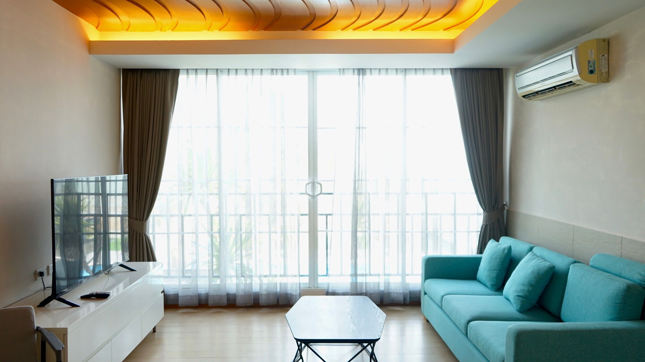 Una sala de estar moderna con un sofá, una mesa de centro, un televisor y un balcón con cortinas.