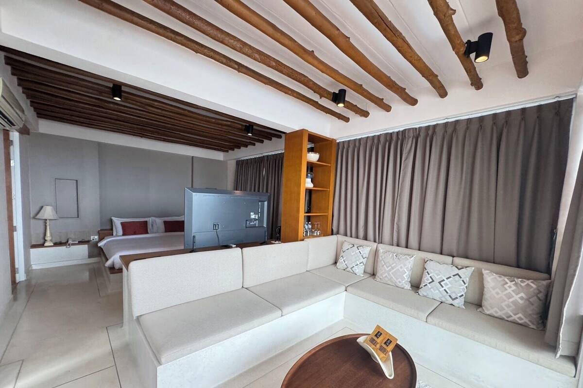 Une chambre d’hôtel moderne dotée d’un grand canapé, d’une télévision, d’une étagère en bois et d’un coin repas avec une table ronde.