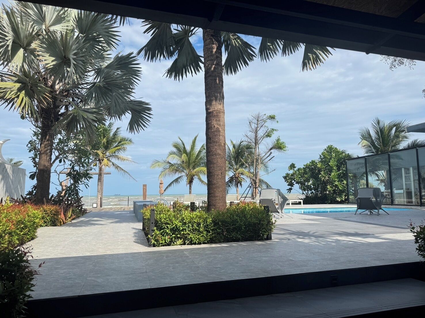 Zona junto a la piscina con palmeras, cielo despejado y vista al océano.